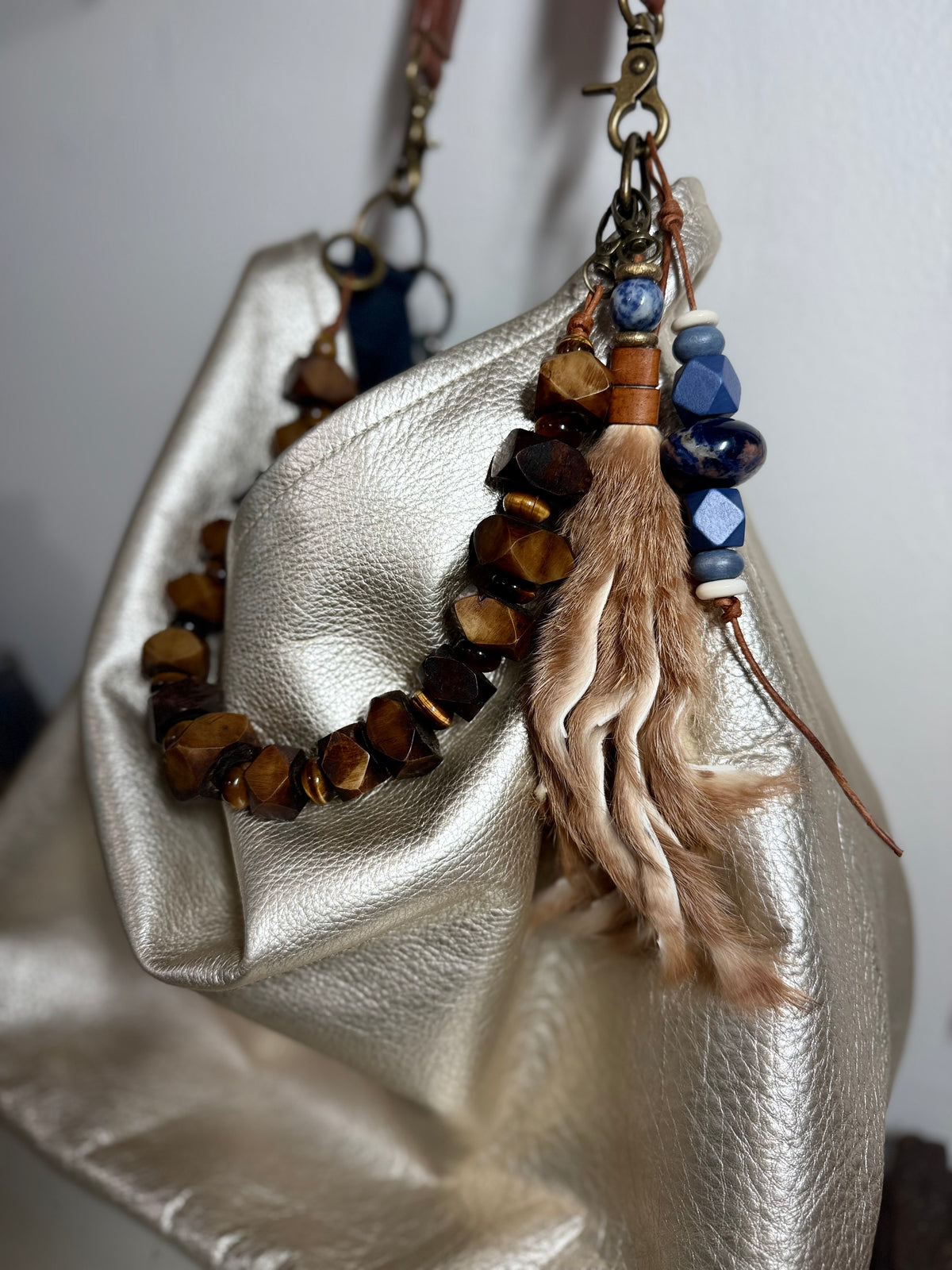 A close-up of  a blonde  fur tassel, and a chunky leather necklace detail. bag charm