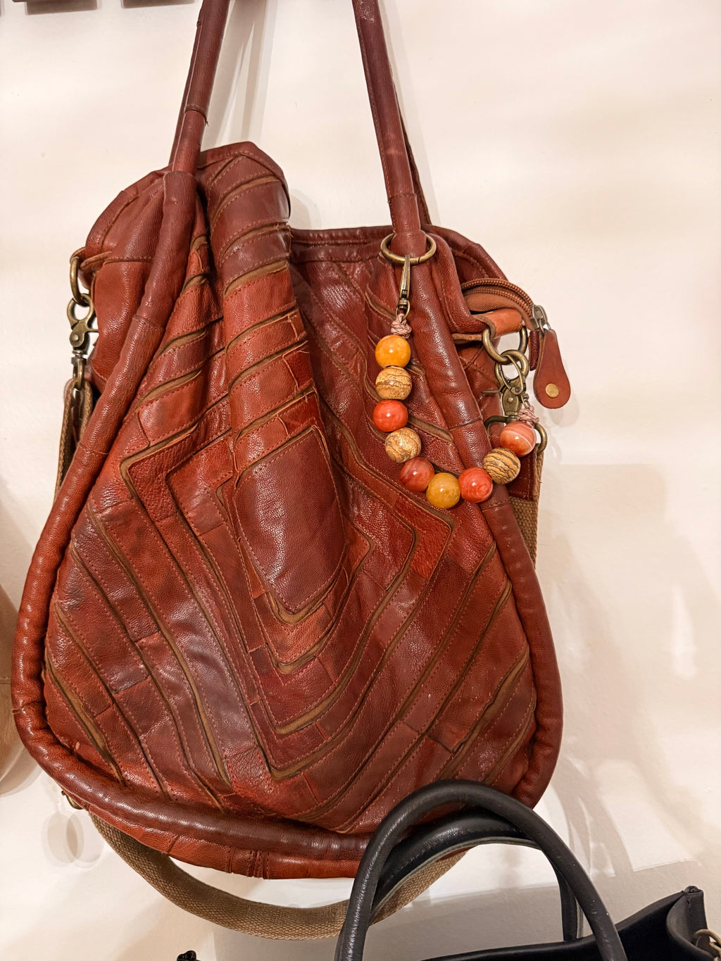 A brown leather hobo shoulder bag with quilted chevron stitching, featuring a beaded wooden keychain charm, displayed against a light background.