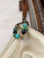 A beaded bracelet with round stones in light blue, mint green, dark navy, and a speckled beige stone, draped over a shiny cream leather surface.
